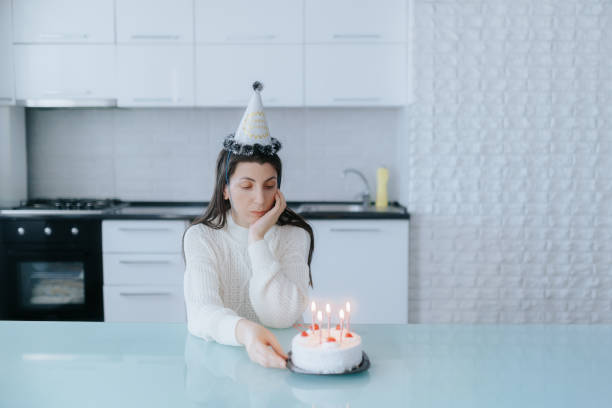 istock Reflective woman sits with birthday cake in a clean, modern kitchen. 2189154351