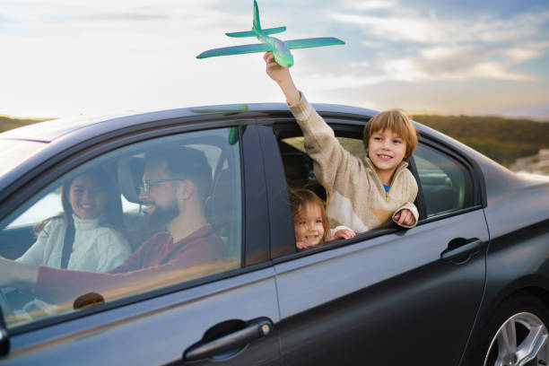 A happy boy plays with a toy airplane while traveling by car with his sister and parents