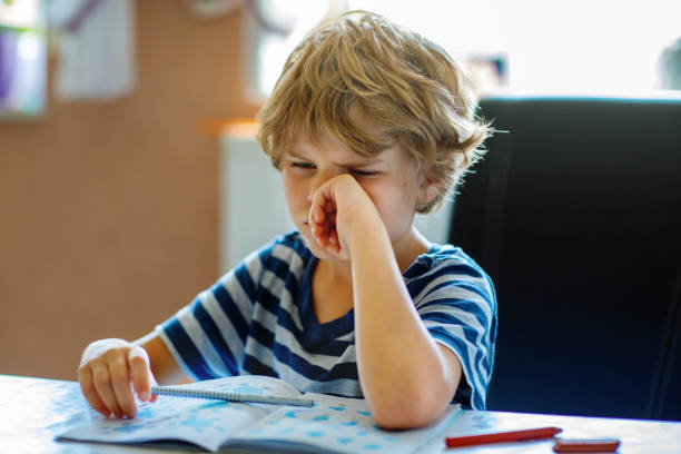 istock Portrait of tired upset boy doing homework in kitchen at home. Elementary school studing writing and learning. Sad and angry child. 2189157731