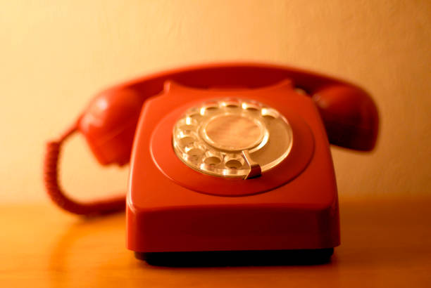 A retro red telephone handset on a table in warm domestic lighting. 1960s, 1970s, 1980s