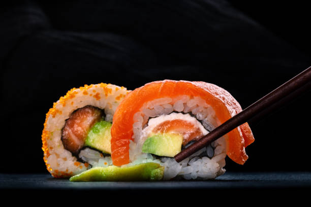 istock Two sushi rolls with salmon and avocado, on a black background with chopsticks 2189166239
