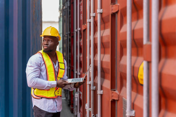 istock african man in safety gear and hardhat using tablet computer at container cargo,foreman checking electronic seal on container box,worker working in shipping yard 2189166553