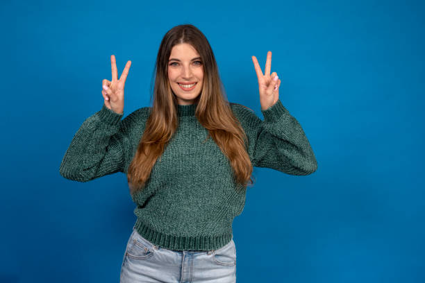 istock Young woman showing victory sign with both hands on blue background 2189166894