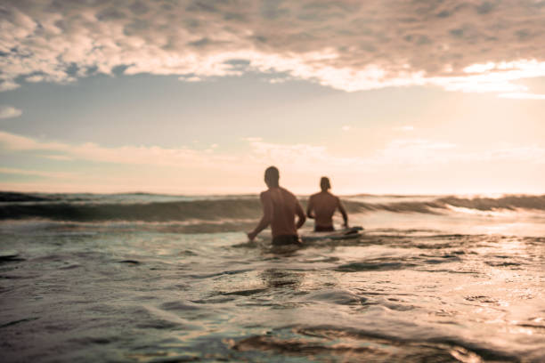 Caucasian male surfers skillfully ride the waves at sunrise, wearing swimwear and using surfboards on an ocean beach. Their adventure highlights the exhilarating action and beauty of outdoor water sports in nature's serene morning light.