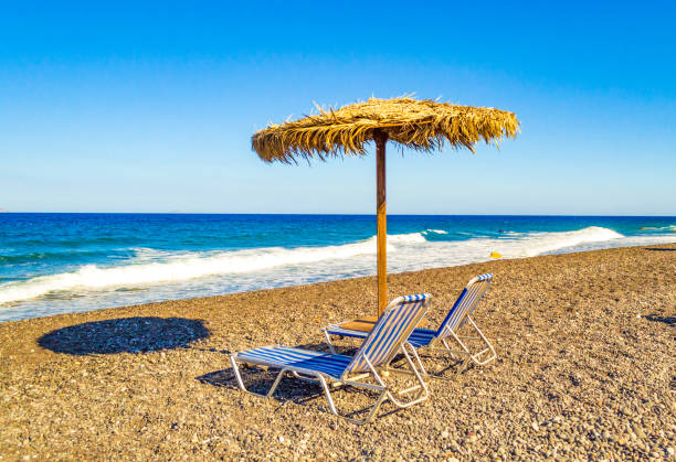 reed umbrella and two empty sunbeds at the Aegean sea coast , Black Beach composed of volcanic sand and pebbles in Kamari village.recreation concept ,Kamari village Santorini island Greece.Picture taken on September 4th,2013