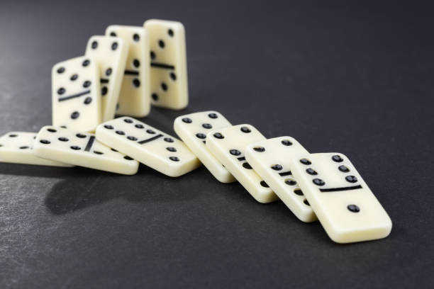 istock Domino effect concept with white dominoes pieces row falling on dark background. 2189173301