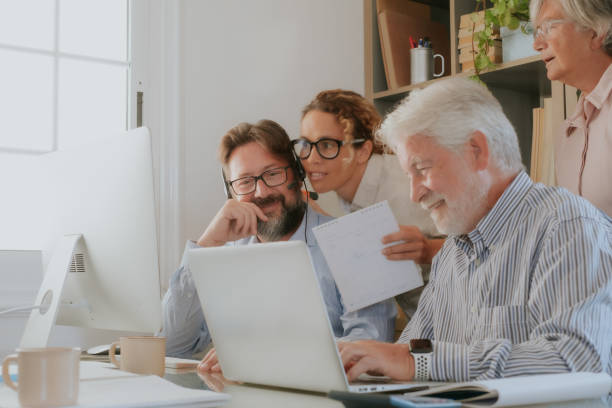 istock Group of old and middle age business people working and using computer and laptop while sitting at the office desk together discussing project details and opinions 2189174251
