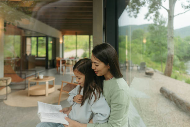 istock Mother and daughter reading together by the window 2189176741