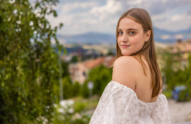 Beautiful woman posing gracefully on a balcony, dressed in a white, flowing off-shoulder dress