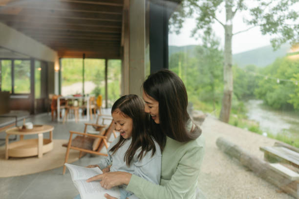 istock Mother and daughter reading together by the window 2189176900