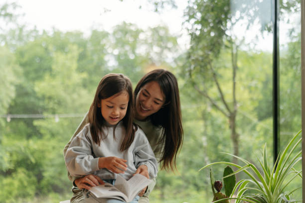 istock Mother and daughter reading together by the window 2189176941
