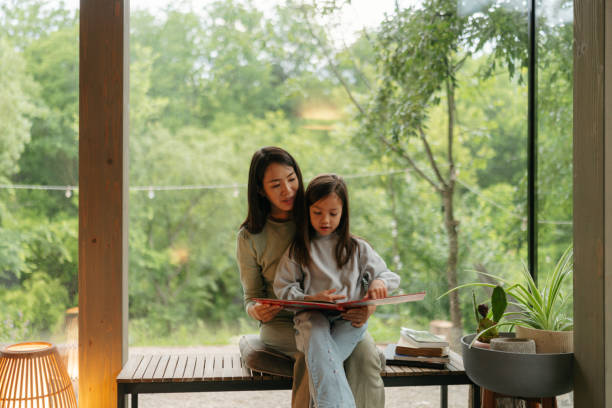 istock Mother and daughter reading together by the window 2189177012