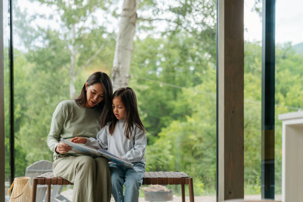 istock Mother and daughter reading together by the window 2189177014