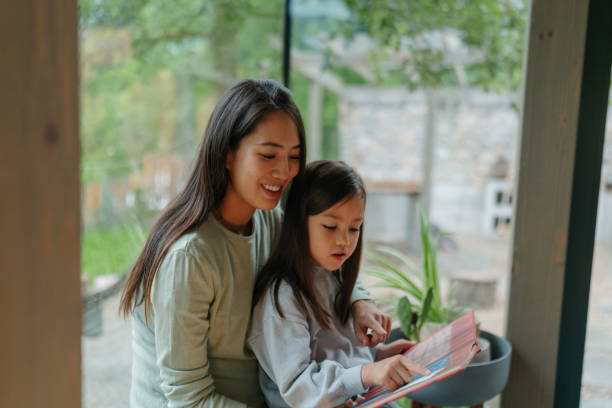 istock Mother and daughter reading together by the window 2189177017