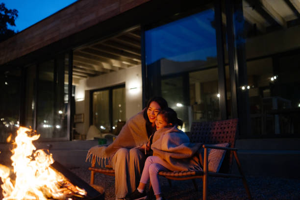 Photo of a heartwarming moment of a mother and daughter sharing a cozy evening by the fire at dusk, right in front of their charming vacation home, embraced by the beauty of nature as they share tender hugs and loving kisses