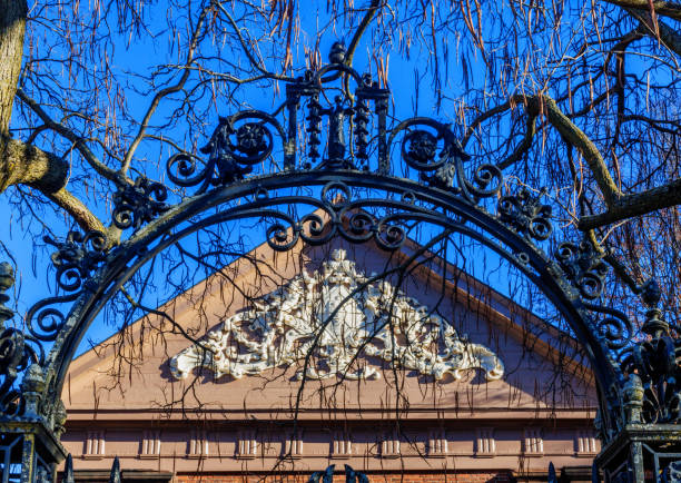 Cambridge, Massachusetts, USA - December 3, 2024: The top of an iron gate to Harvard University's Harvard Yard. The gate was donated by the Harvard Class of 1870. The gate leads to the small Holden Chapel building with its decorated roof peak. Completed in 1744, the Chapel is the oldest building at Harvard and one of the oldest college buildings in America.