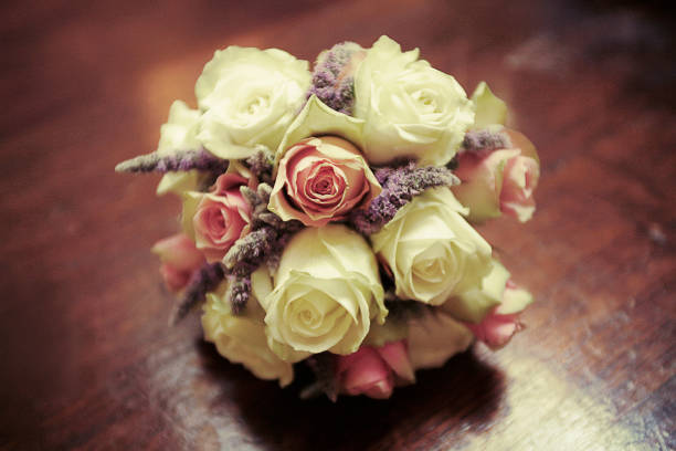 A wedding bouquet with white and pink roses resting over a wooden table. Shot with natural light