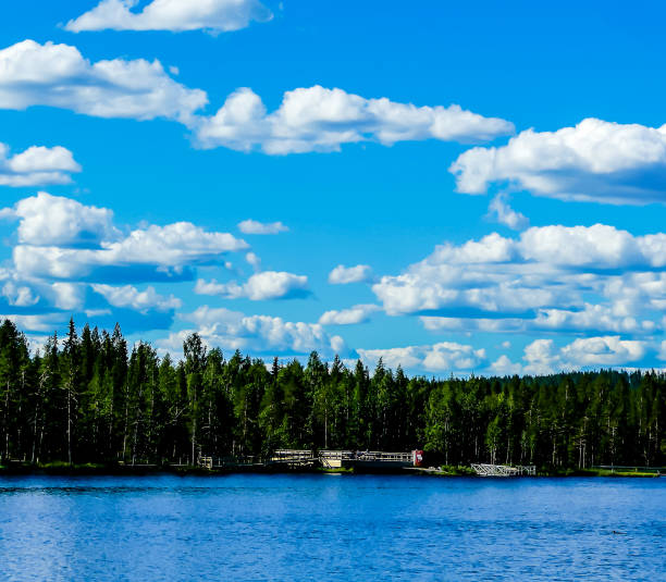A beautiful blue sky with clouds and a lake in the background. The lake is surrounded by trees and a small town