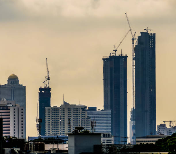 A city skyline with a cloudy sky and a crane in the background. The buildings are tall and the sky is overcast