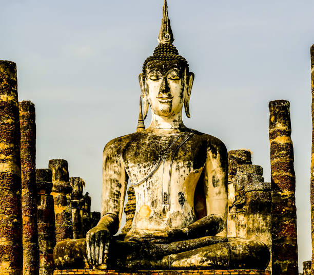 A statue of a Buddha sitting in a temple. The statue is surrounded by pillars and is the main focus of the image