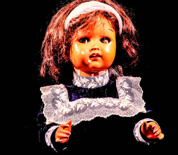 A doll with a white band around her head and a black dress. The doll is looking down and he is sad