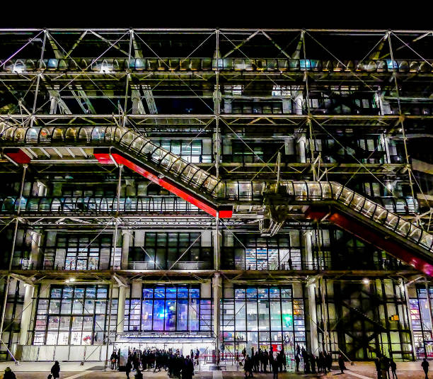 A large building with a red escalator in the middle. The building is lit up at night