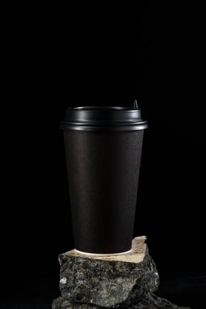 istock Black coffee cup stands on a textured rock surface against a dark background 2189198331