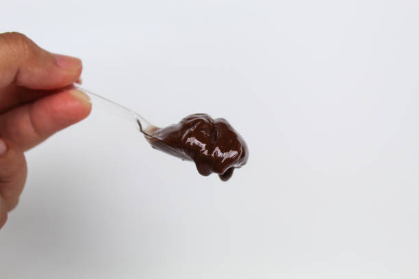 A small square bowl of chocolate sauce. The bowl is made of glass and is sitting on a white background