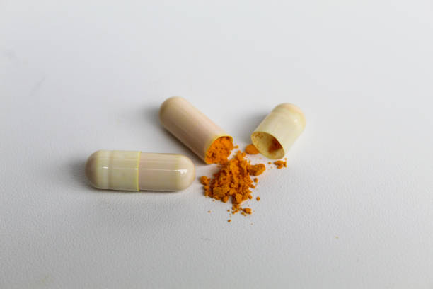 Opened capsule with yellow turmeric powder filling inside. Isolated on white background