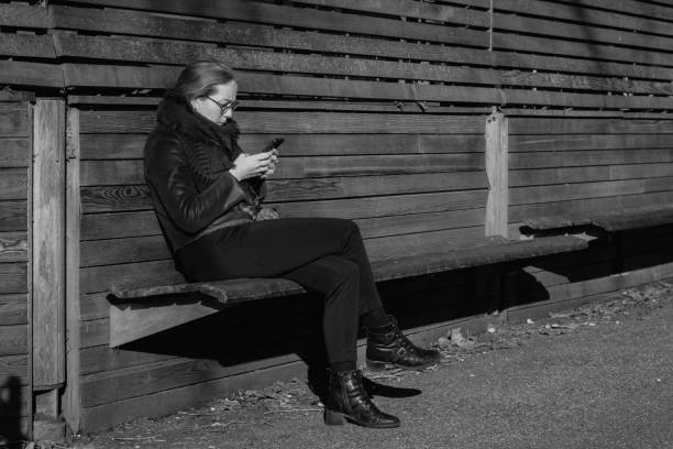 London, England, UK – January 15, 2024: A woman sits alone on a wooden bench in a London park during winter. The textured background of wooden panels adds warmth to the cold ambiance, and her contemplative posture brings a sense of introspection and calm.