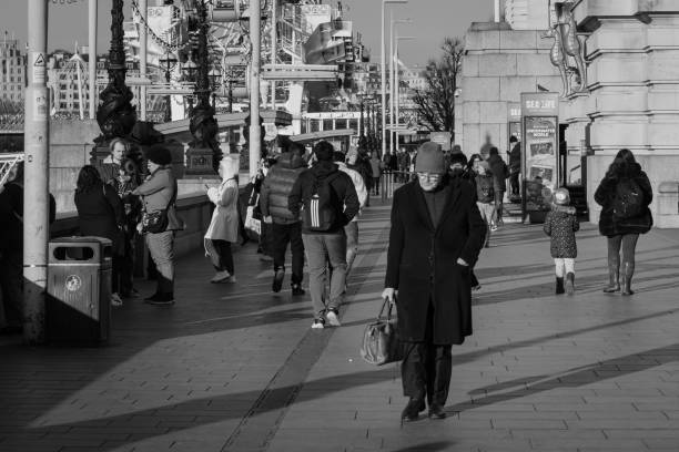 London, England, UK – January 15, 2024: A bustling scene of pedestrians on the South Bank of London. The crowd features people of various walks of life, including a man walking thoughtfully with a bag. The winter sun casts long shadows, adding a contemplative mood to the busy urban environment.
