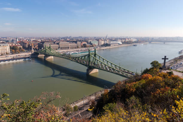 Budapest, Hungary - April 2025 The iconic Elizabeth Bridge, a historic bridge painted in green, stretches across the Danube River in Budapest, Hungary. Featuring intricate ironwork, tall gothic-style towers topped with statues, and vintage street lamps along its railings, the structure connects the Buda and Pest sides of the city. The river flows calmly below under an overcast sky, with a few distant pedestrians visible on the bridge. This image captures the architectural grandeur and engineering marvel of the 19th-century landmark on a cloudy daytime in autumn or spring. Ideal for commercial use in travel magazines, tourism campaigns, historical documentaries, urban planning articles, and European architecture features, highlighting Budapest's skyline and riverfront heritage.