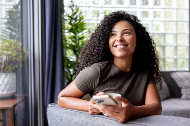 istock Thoughtful woman at home drinking coffee while using her phone 2189234783