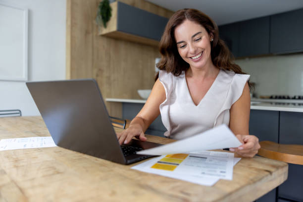 istock Happy woman at home paying bills online using her laptop 2189234789