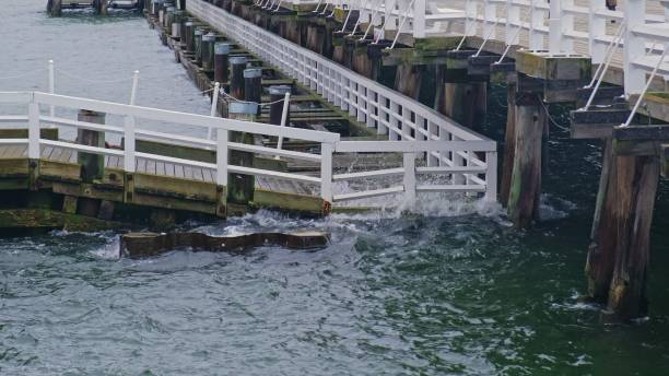 Sea Waves Splashing Against Metal Break Water Barrier Protecting Wooden Pier Deck during Windy Day Autumn Storm Season