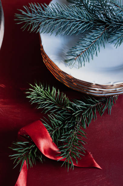 One gray plate with a knife and fork in a mini Santa Claus hat stand on a beautifully served holiday table with a red tablecloth and green tinsel on a winter evening in the kitchen, side view close-up with selective focus.