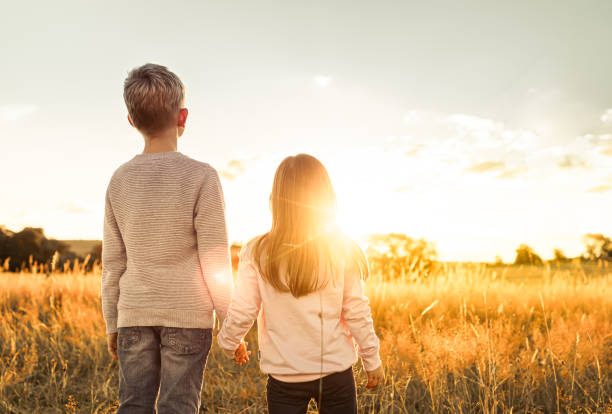 istock Young boy and girl watching beautiful sunset in the meadow. 2189246692