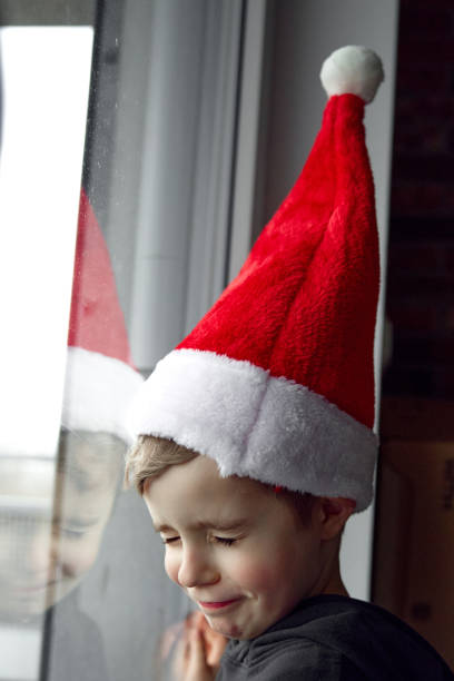 istock Christmas Child Boy in Santa Hat looking out the window 2189252388