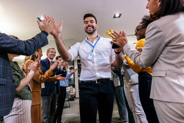 Young businessman receiving prize cup, proud colleagues applauding for him and cheering. stock photo