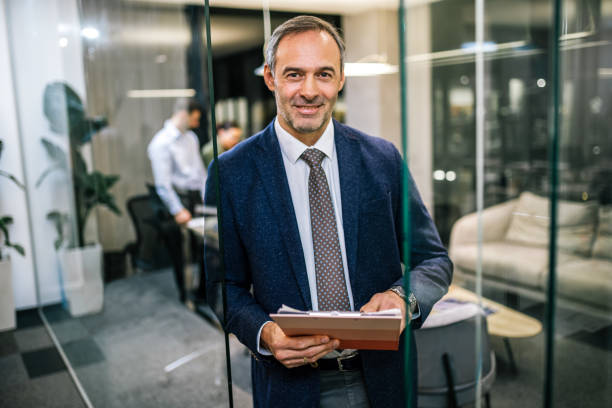 istock Older businessman standing in his office with paperwork. 2189253811