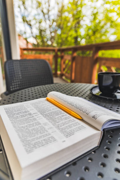 istock Open Holy Bible with yellow pen lying on plastic garden table with black coffee cup standing on balcony with wooden fence and green surroundings 2189259858