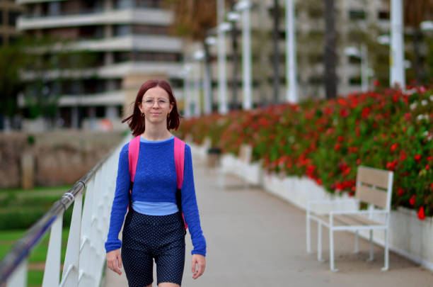 istock A woman wearing a blue sweater and a pink backpack walks down a sidewalk 2189266897