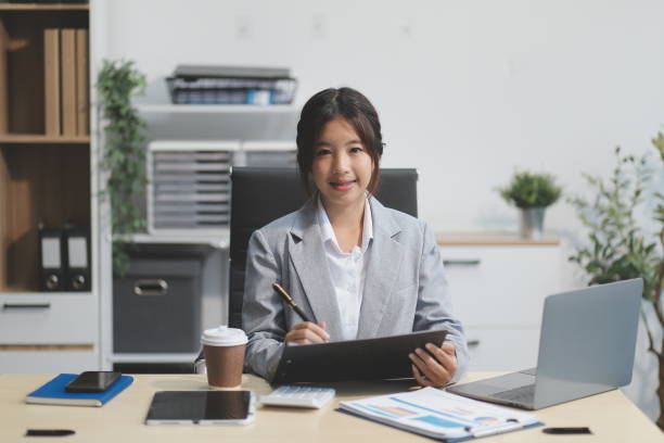 istock Successful Asian businesswoman smiling using laptop computer and holding coffee cup at office. Confident Asia businesswoman sitting happily in the office. 2189274928