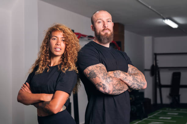 confident muscular sportive instructors standing with crossed arms at gym and looking at camera, concept of fitness and active lifestyle