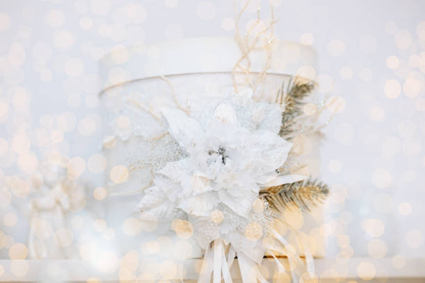 A beautifully arranged white gift box featuring delicate winter decorations such as a poinsettia flower and evergreen accents sits in a cozy setting, evoking the spirit of Christmas and the New Year.