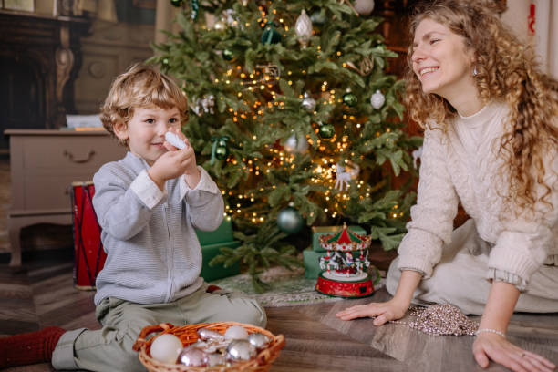 istock Child and parent enjoying holiday decorations by a Christmas tree while preparing for New Year celebrations 2189285463