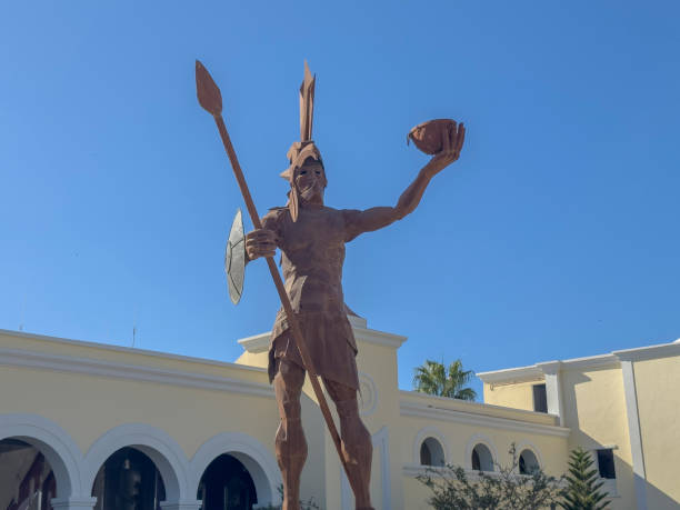 Los Cabos, Baja California Sur, Mexico. Dec 8, 2024. A towering statue of a warrior, clad in armor and holding a spear and a severed head, stands against a backdrop of a clear blue sky.