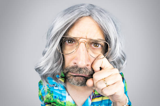 A funny fisheye image of an older gray guy with long hair looking sad as he wipes a tear.