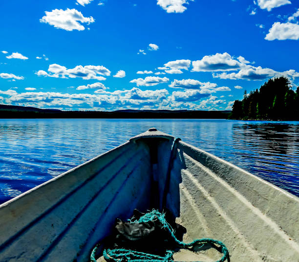 A boat is floating on a lake with a blue sky in the background. The boat is white and has a green rope tied to it. The scene is peaceful and serene, with the water
