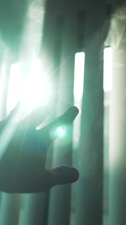 Vertical close up of man hand silhouette reaches for light through the vertical blinds on the window into the dark smoke filled room. Symbolizing hope and salvation in bad times